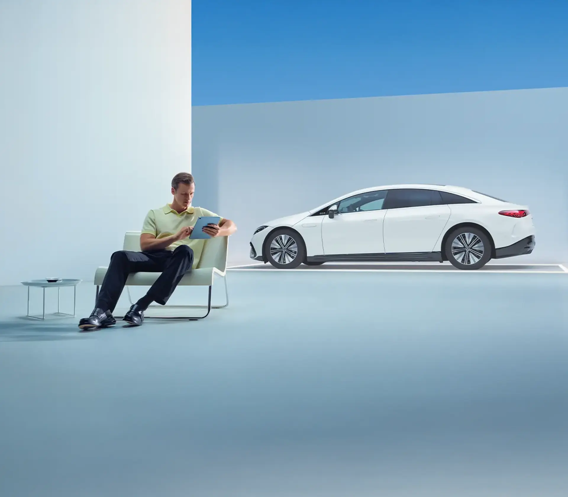 Mann sitzt mit i Pad in der Hand, Auto im Hintergrund