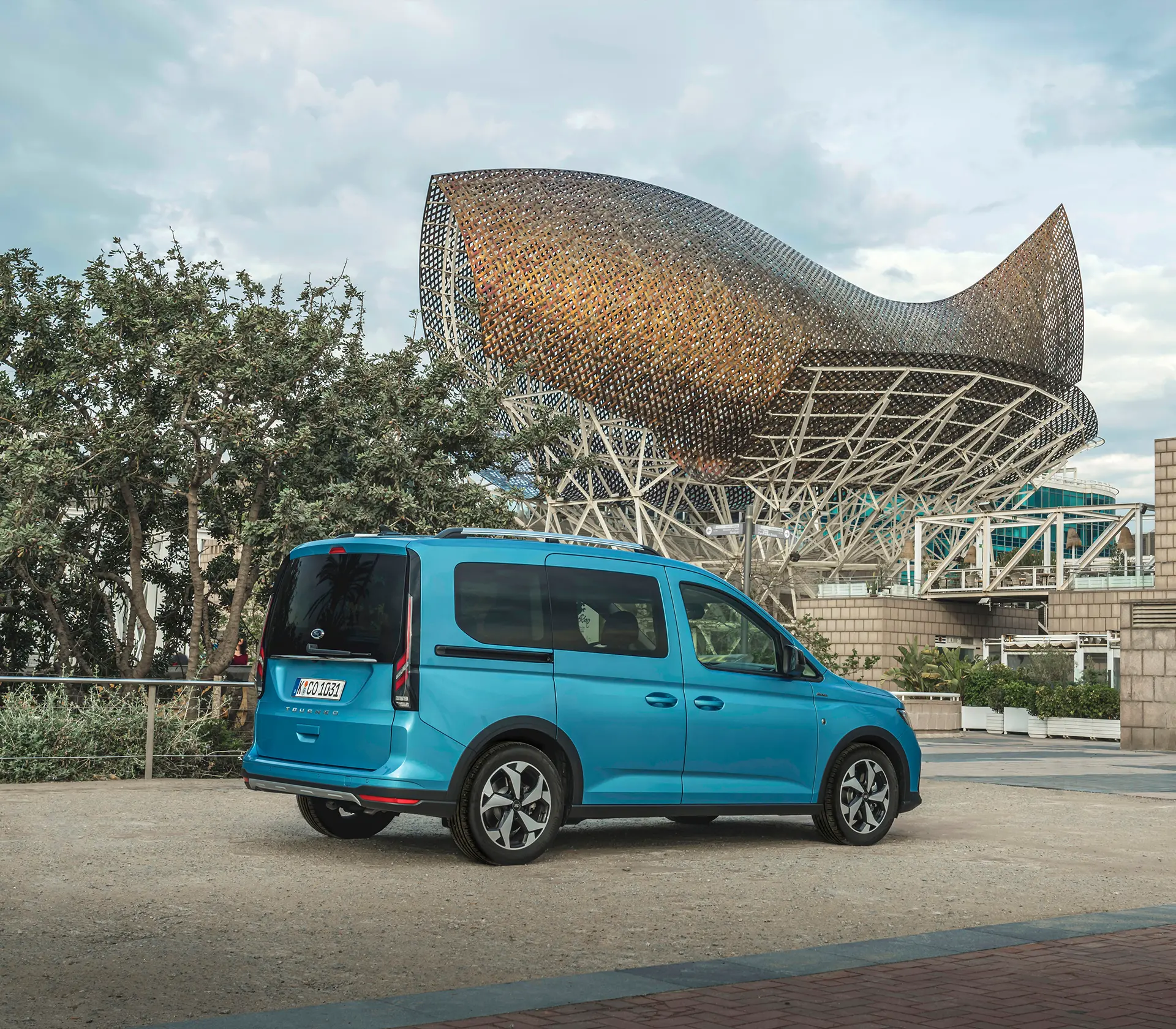 Frontansicht auf den blauen Ford Tourneo-Connect vor Bäumen und einem Gebäude