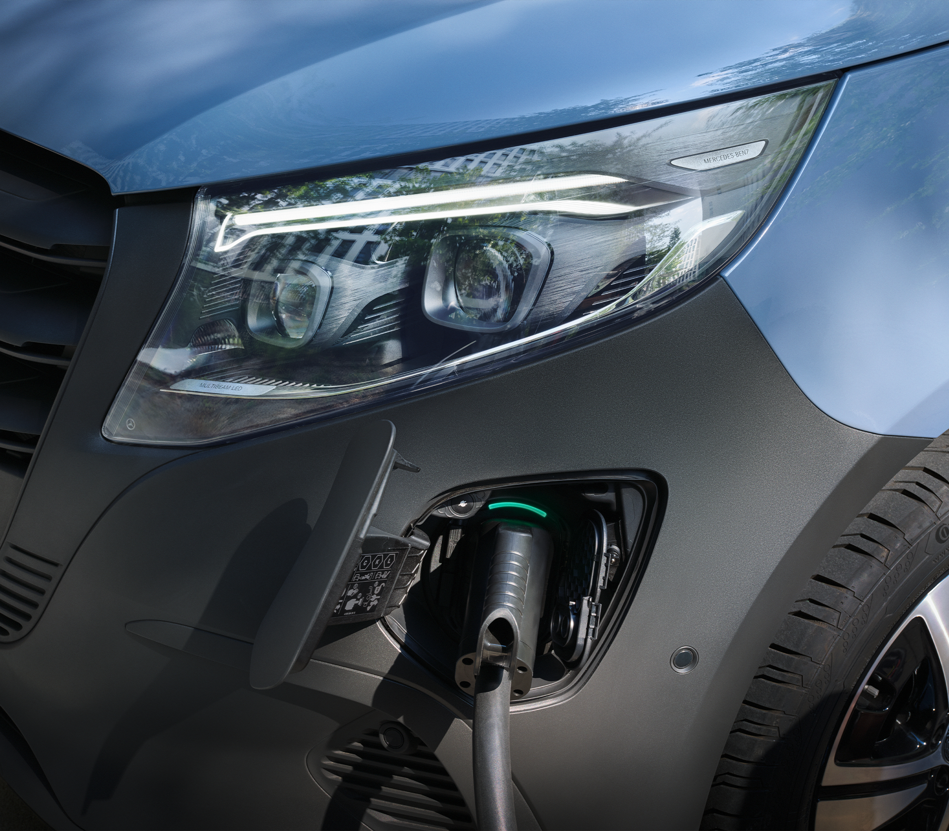 „Nahaufnahme eines Mercedes-Benz Elektrofahrzeugs beim Ladevorgang mit sichtbarem LED-Scheinwerfer und Ladeanschluss.“