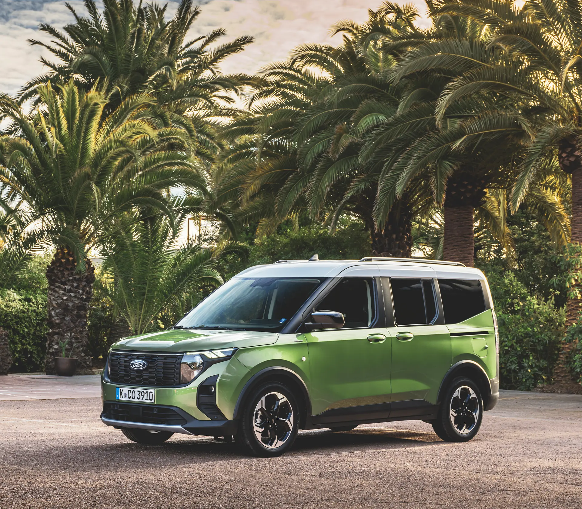 ein grüner Tourneo Courier im Stand von vorne mit Plamen im Hintergrund