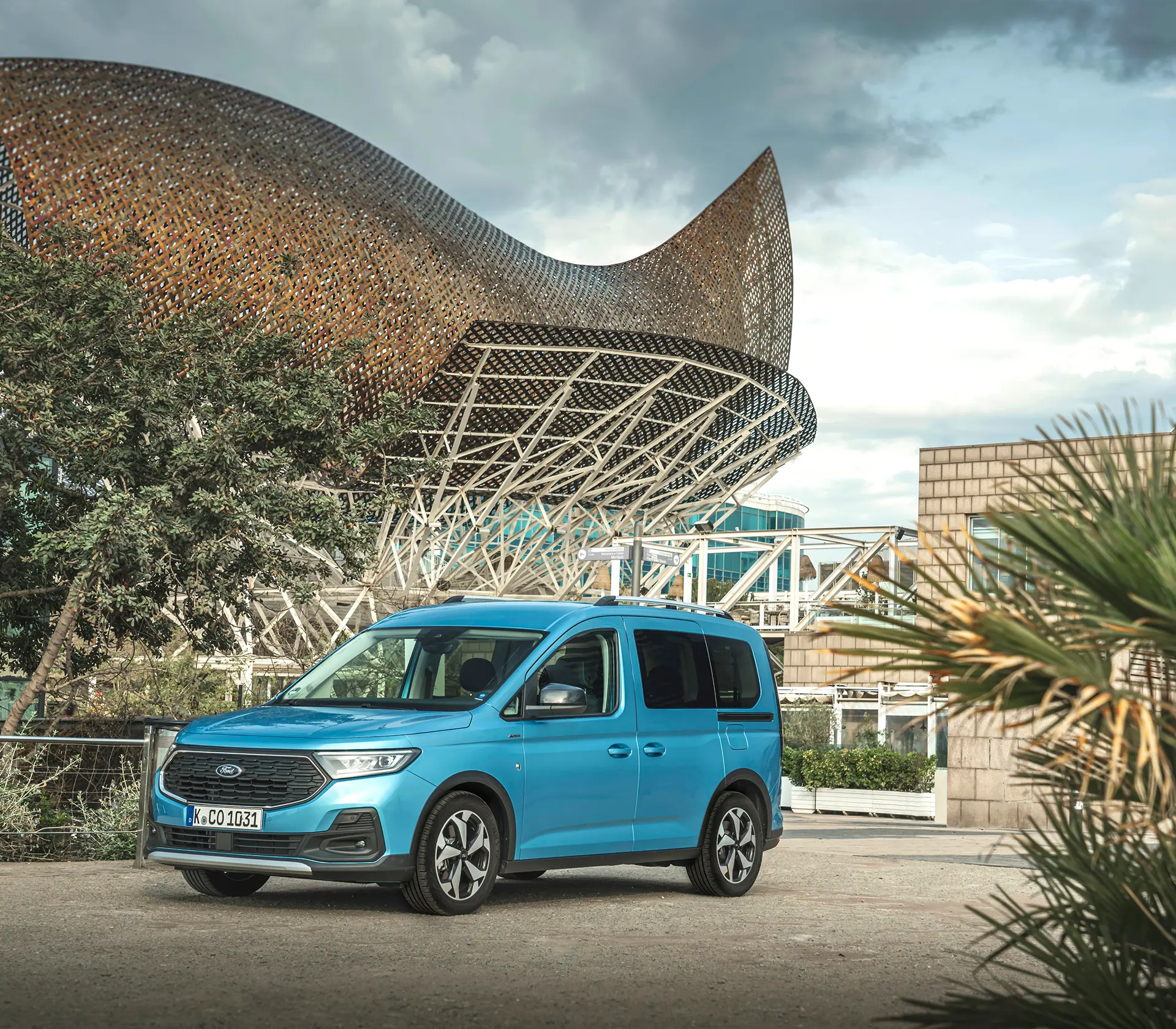 Frontansicht auf den blauen Ford Tourneo-Connect vor Bäumen und einem Gebäude