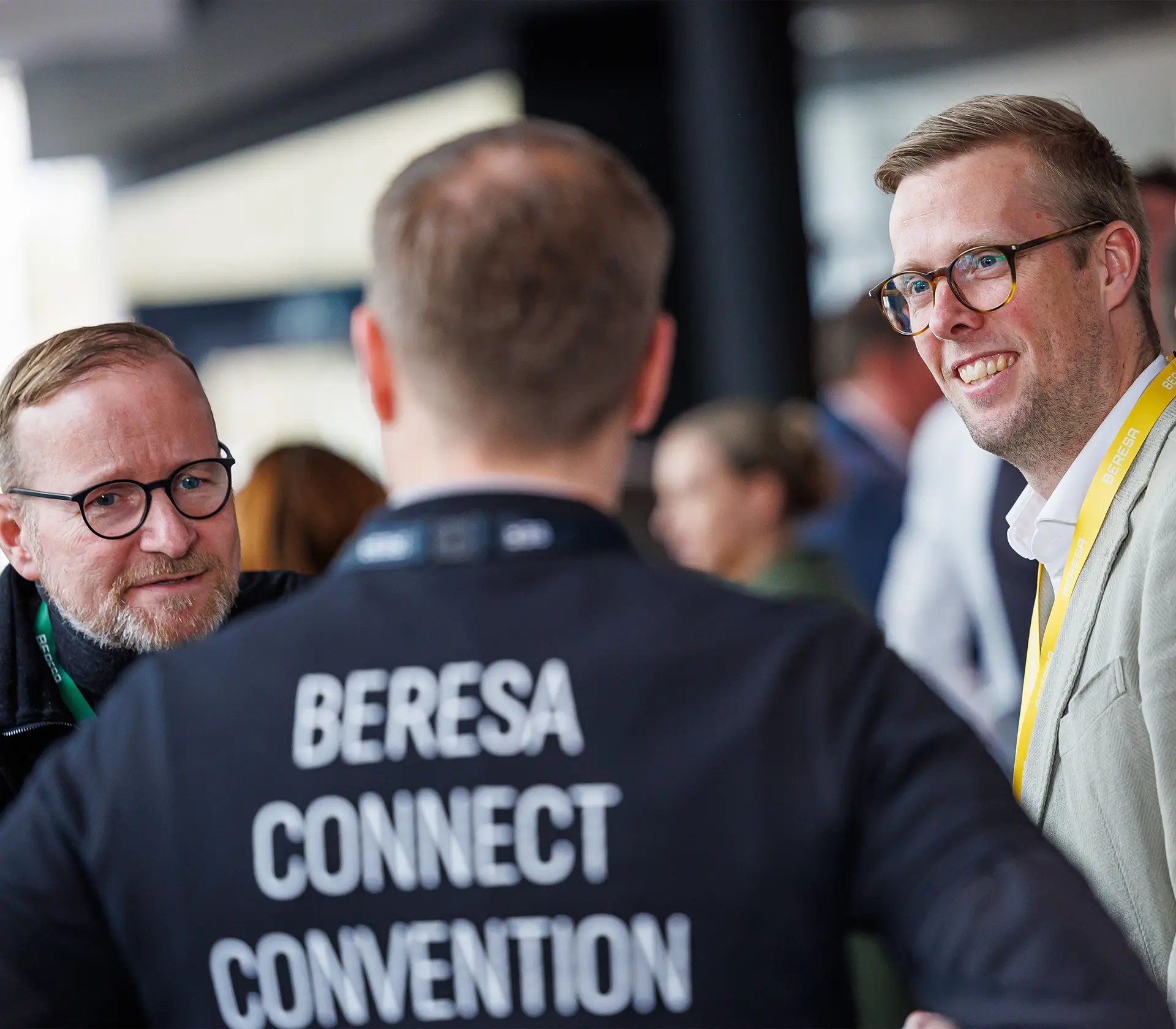 Ein Mann steht in der Mitte des Bildes und auf dem Tshirt auf seinem Rücken steht BERESA Connect Convention und links und rechts von ihm stehen zwei Männer mit denen er sich unterhält