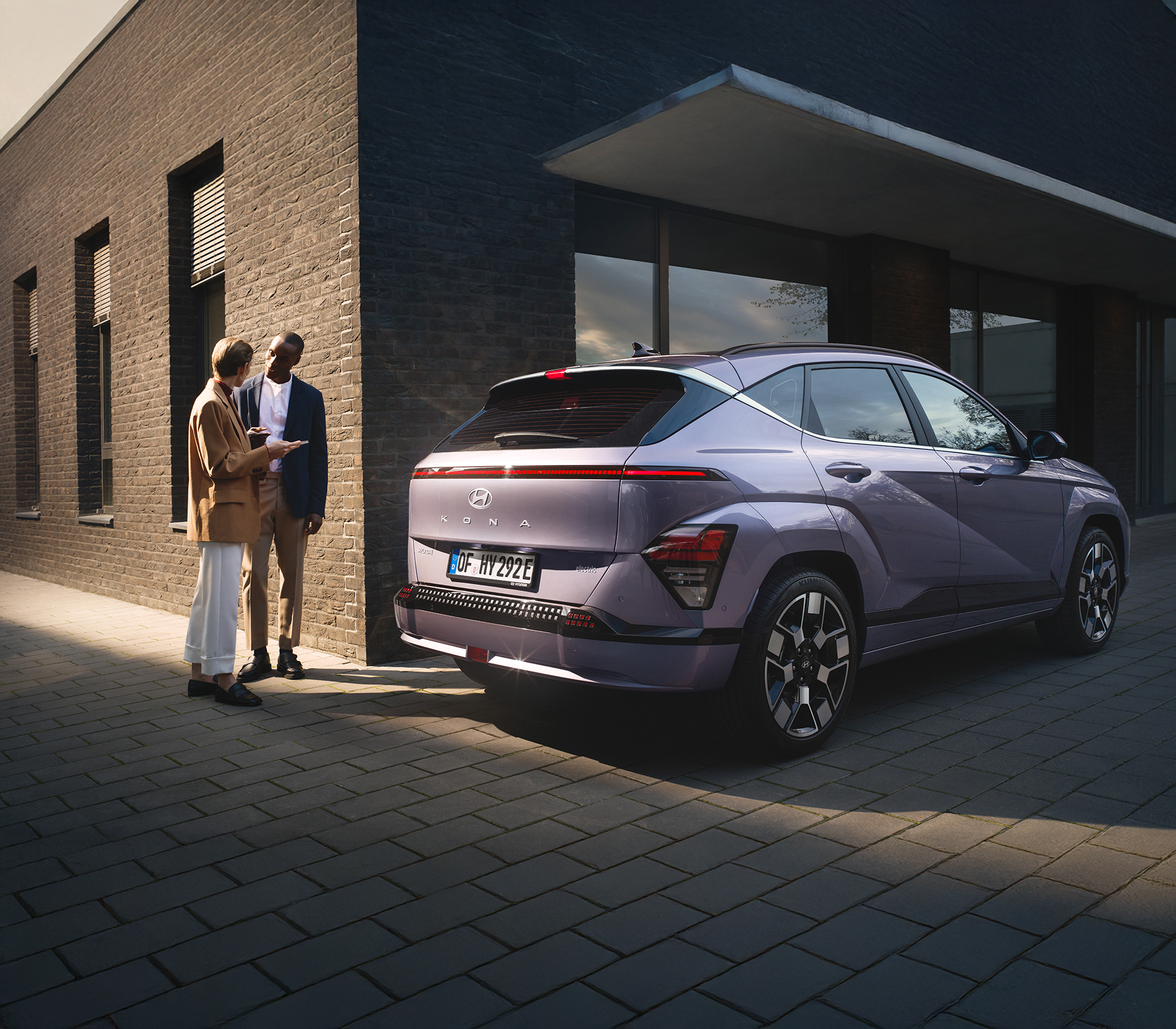 Hyundai SUV Kona elektro geparkt vor einem Gebäude mit zwei Personen hinter dem Auto