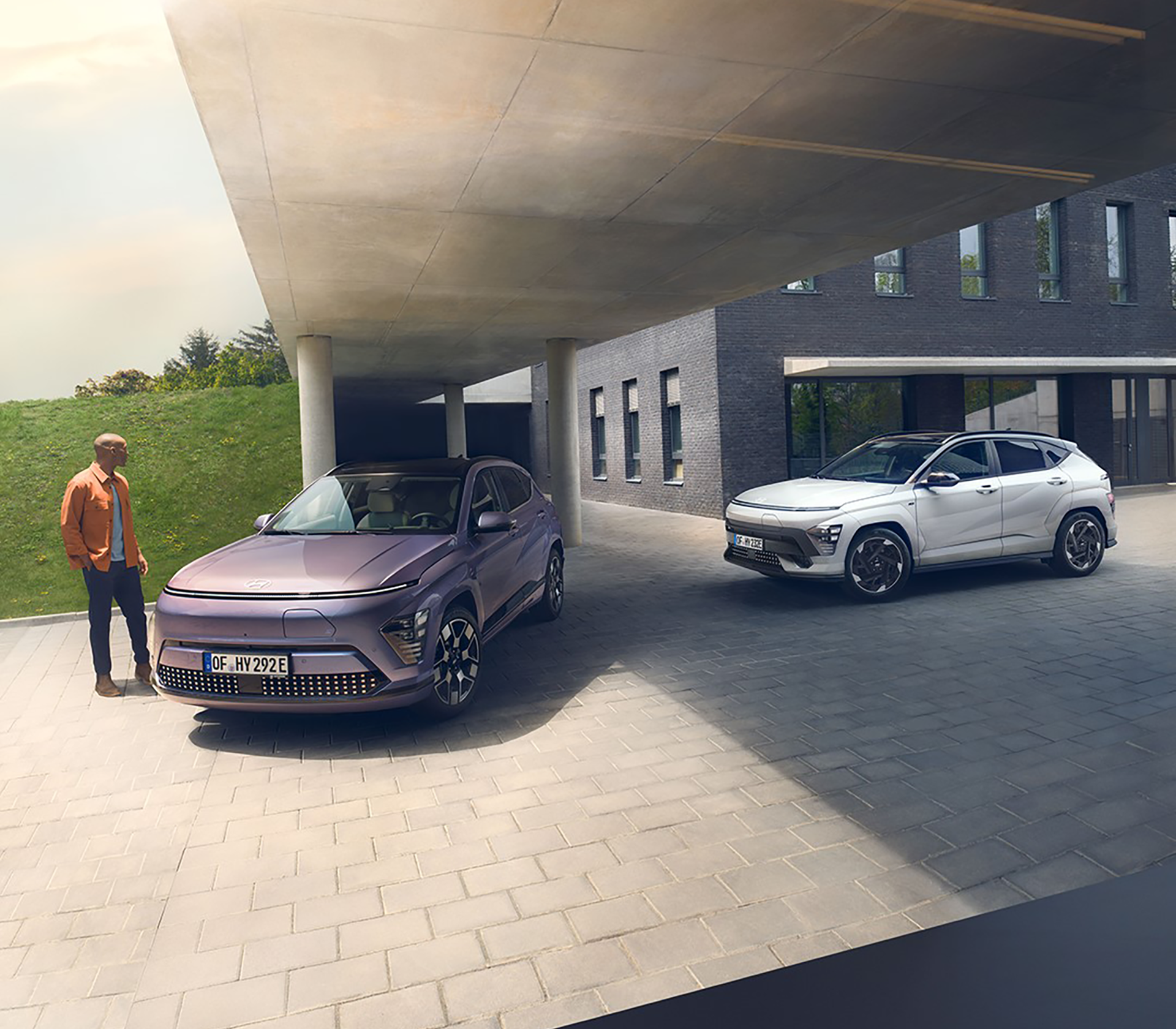 Hyundai SUV Kona elektro geparkt unter dem Dach eines modernen Gebäudes, ein Mensch steht daneben und hinter dem vorderen Auto steht noch ein weißer Hyundai Kona elektro