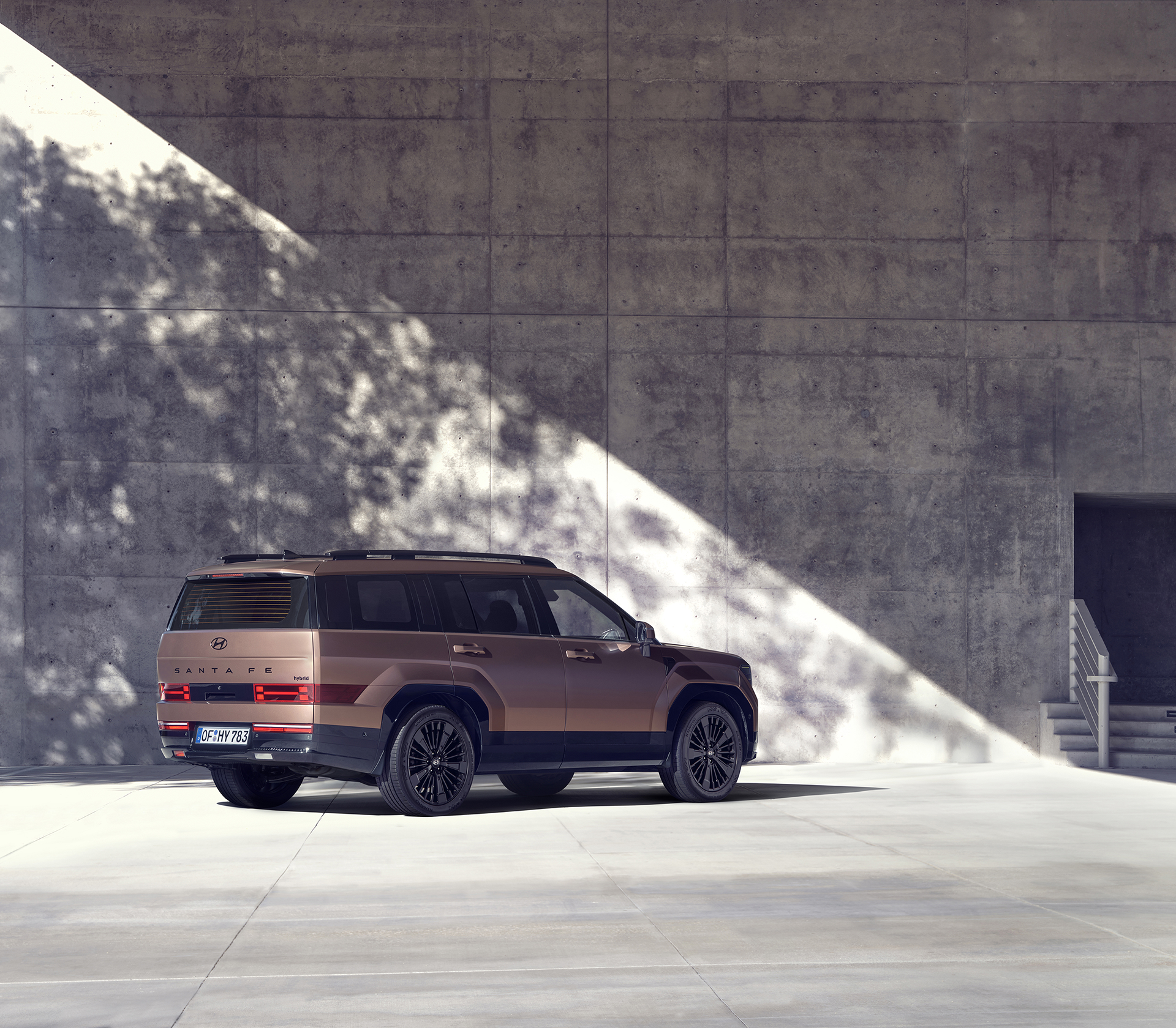 Hyundai SANTA FE schräg von hinten und der Seite vor einer grauen Mauer mit Schatten eines Baumes