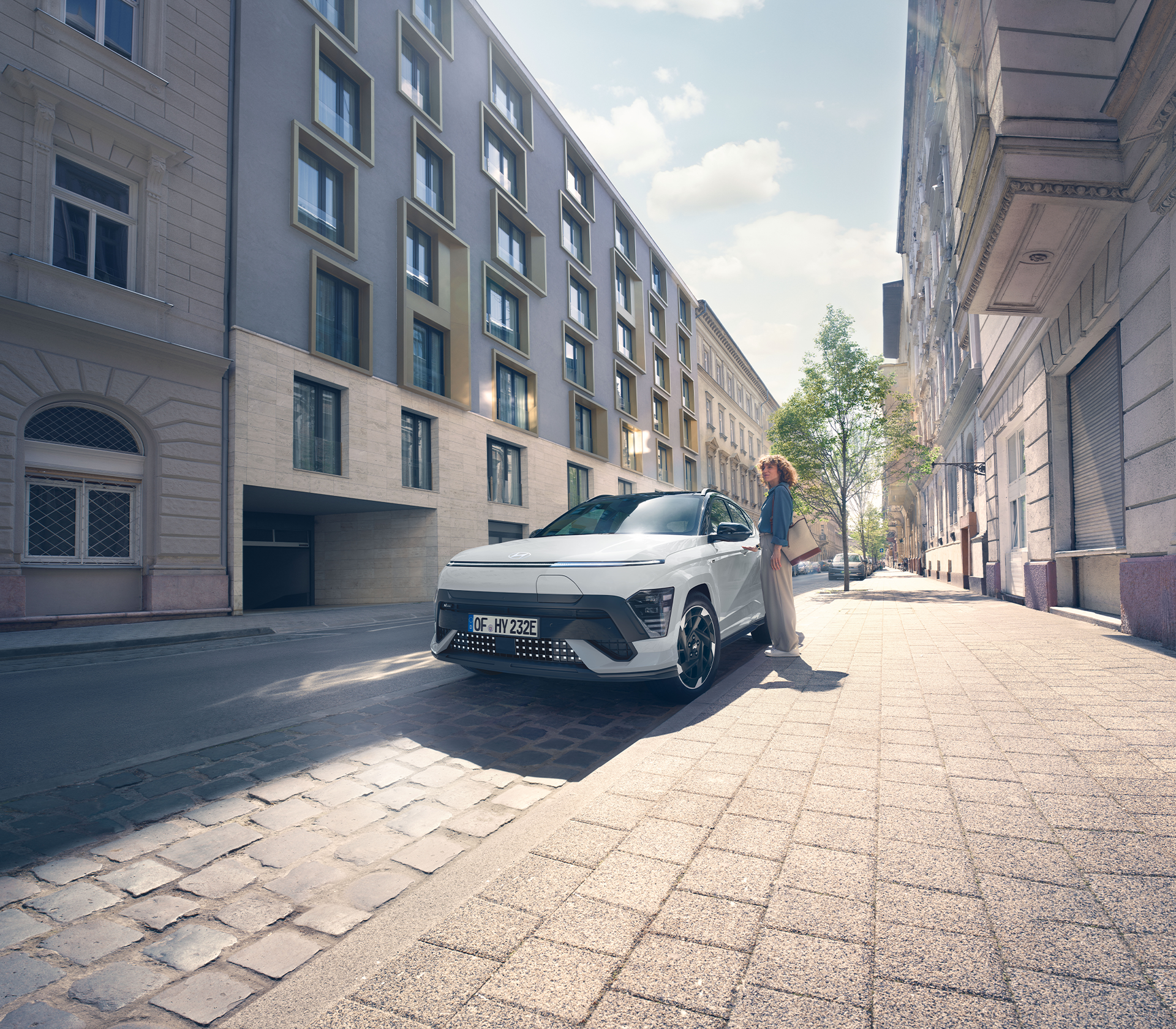 Hyundai SUV Kona elektro  steht am Straßenrand in weiß mit einer Person daneben, drum Herum sind hohe Gebäude