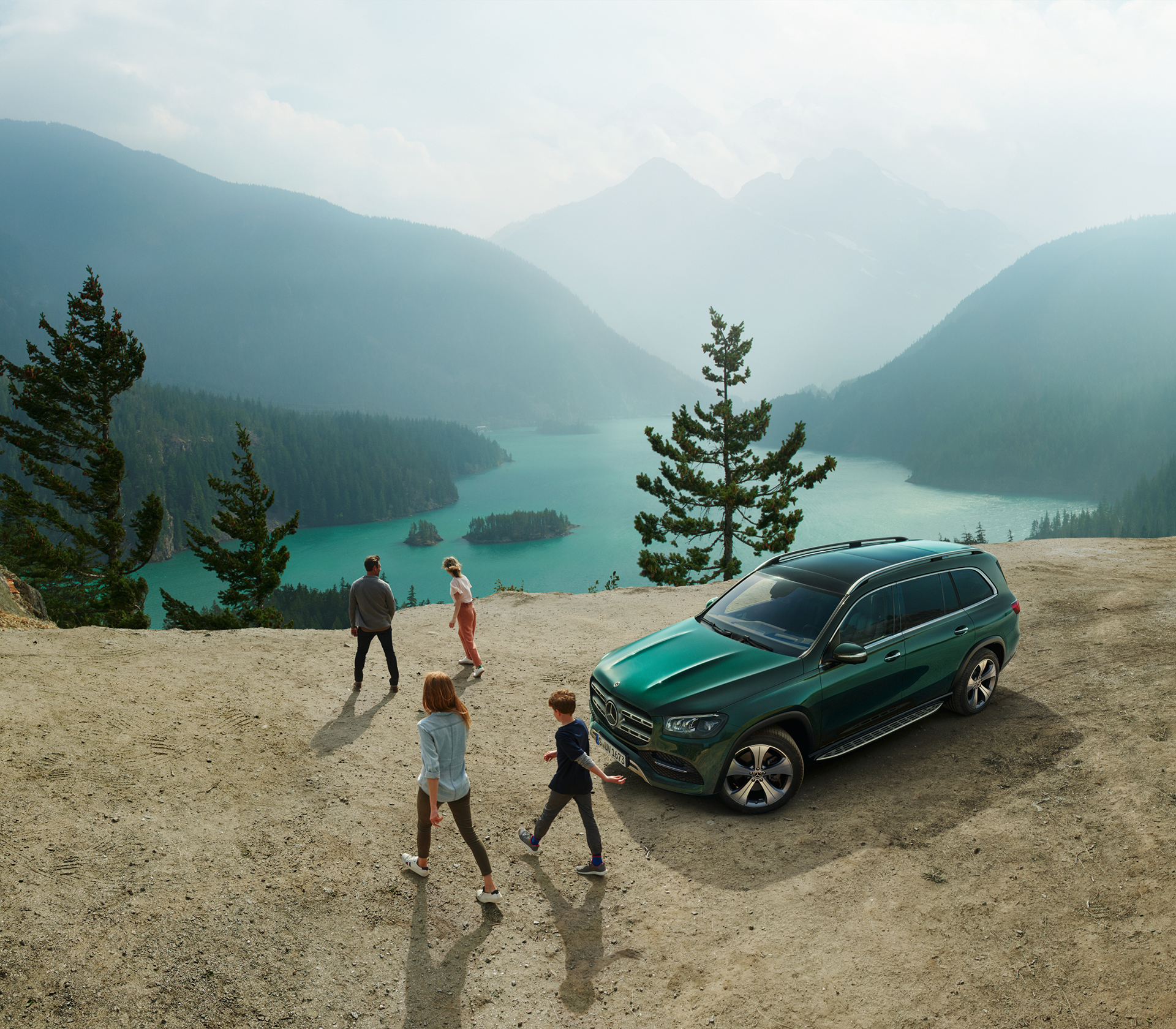 Mercedes-Benz GLS HEckansicht und von der Seite steht geparkt vor einem See mit Bäumen und Bergen im Hintergrund, man sieht vier Menschen die von dem Auto weg laufen