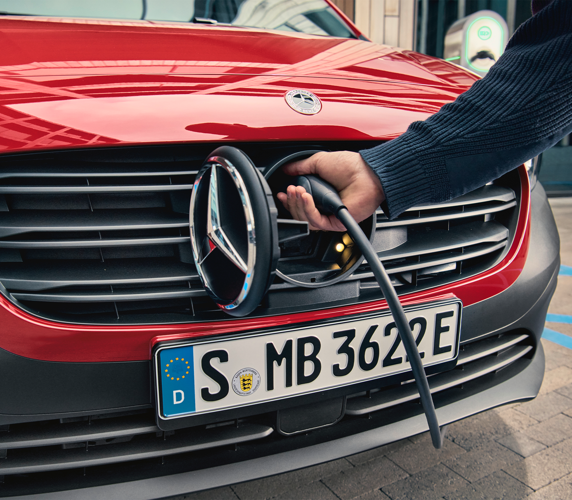 Nahaufnahme des Ladevorgangs beim Mercedes-Benz eCitan, bei dem das Ladekabel hinter dem markanten Mercedes-Stern im Kühlergrill angeschlossen wird.