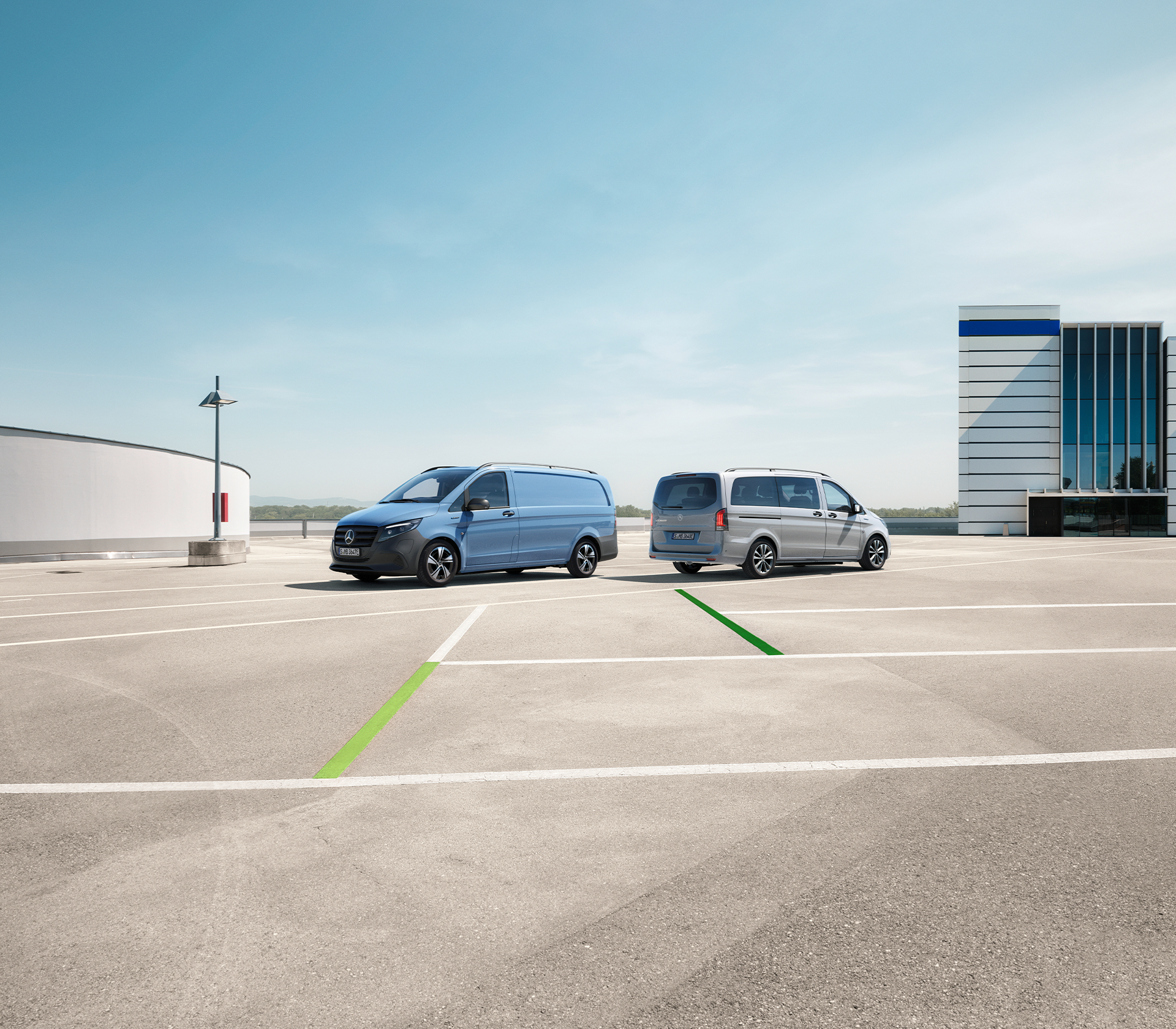 Zwei Mercedes-Benz eVito Modelle – einer in Blau, einer in Silber – parken auf einem offenen Areal mit moderner Büroarchitektur im Hintergrund.