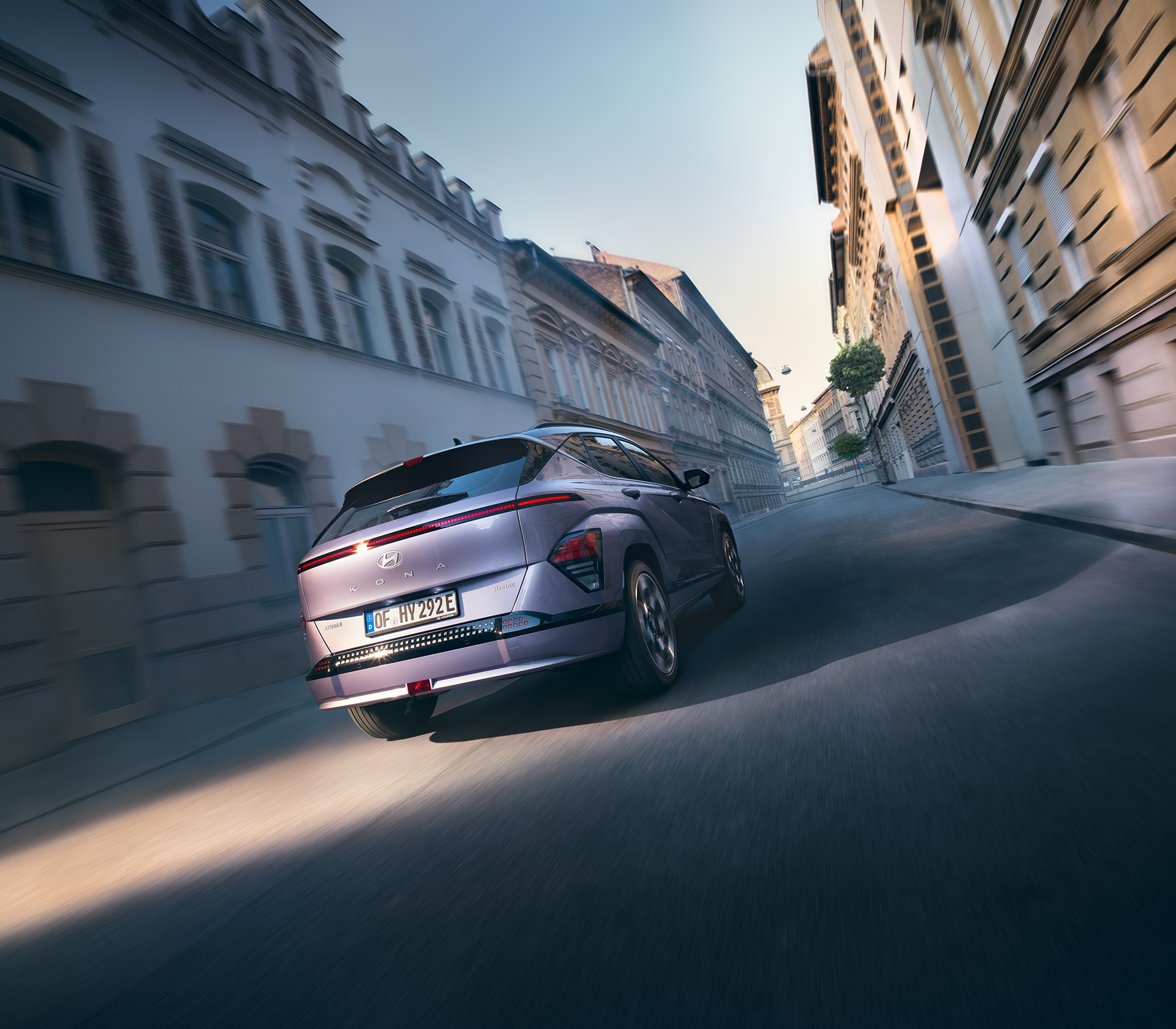 Hyundai SUV Kona elektro fährt auf der Straße mit Gebäuden drum herum, Heckansicht