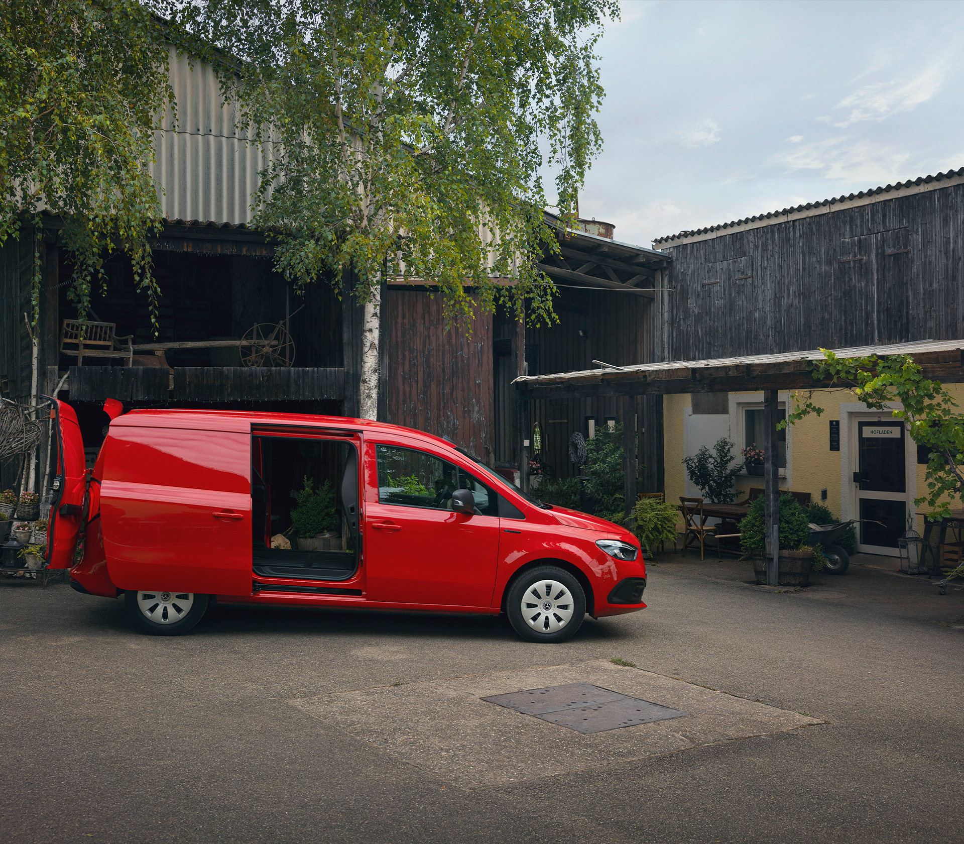 Roter Mercedes-Benz Citan mit geöffneter Seitentür vor einem ländlichen Hof – ideal für Handwerk und Lieferdienste.