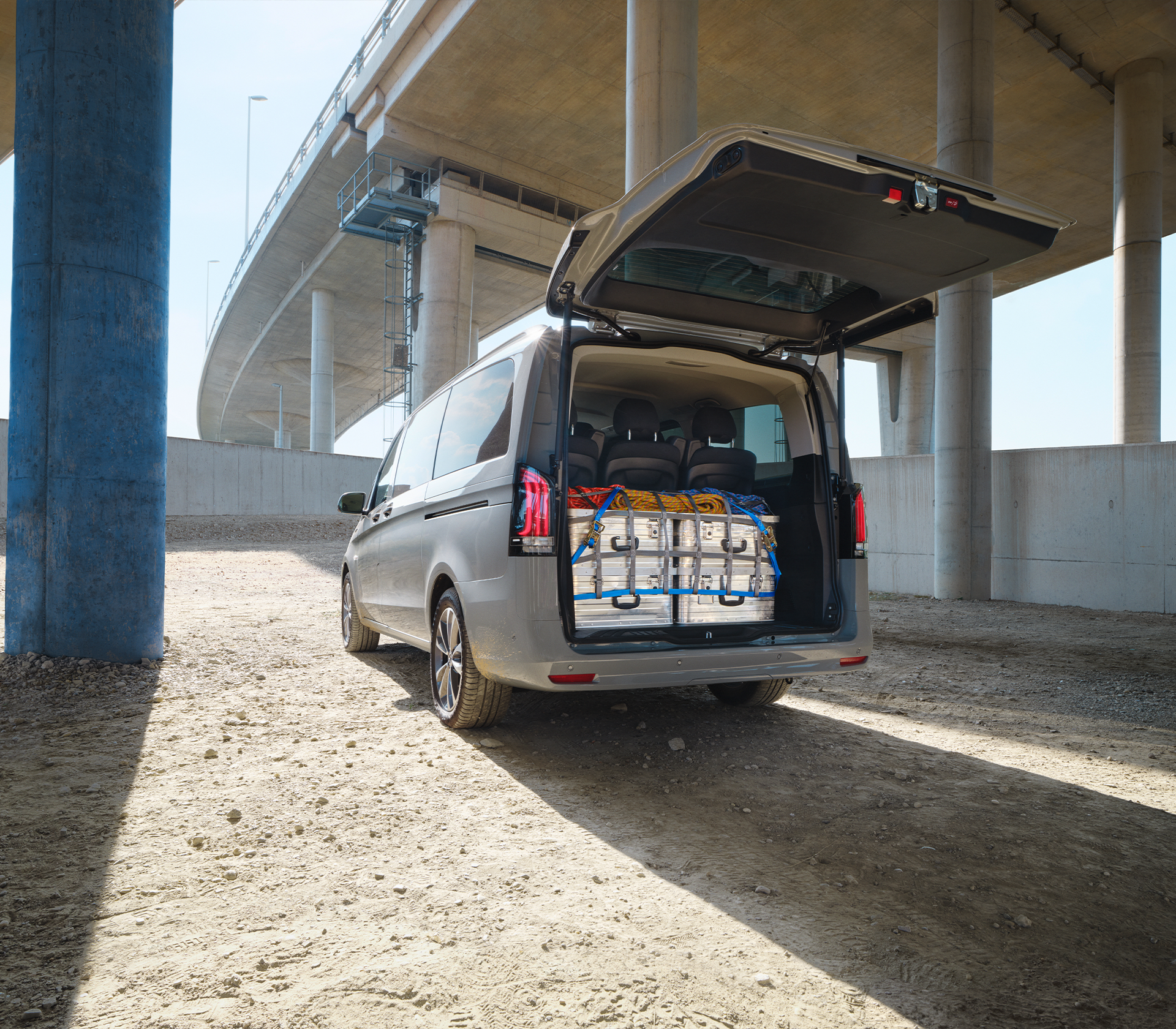 „Mercedes-Benz e-Vito mit geöffneter Heckklappe unter einer Brücke, beladen mit Transportboxen und Gepäck.