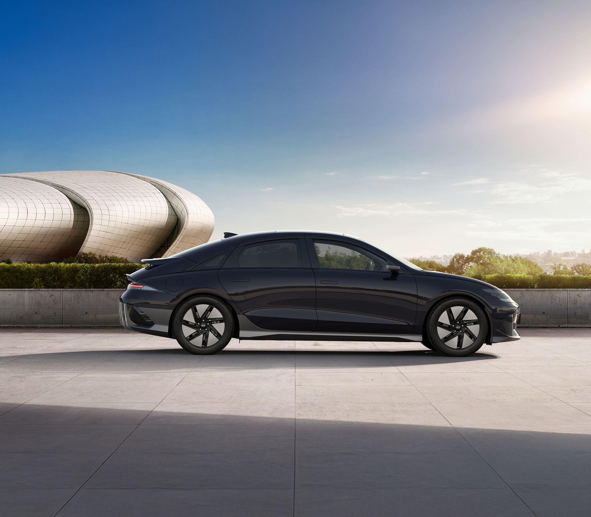 Hyundai IONIC 6 Heckansicht in schwarz, Hintergrund Himmel, Bäume und ein modernes Gebäude von der Seite mit einem modernen Gebäude im Hintergrund und blauem Himmel