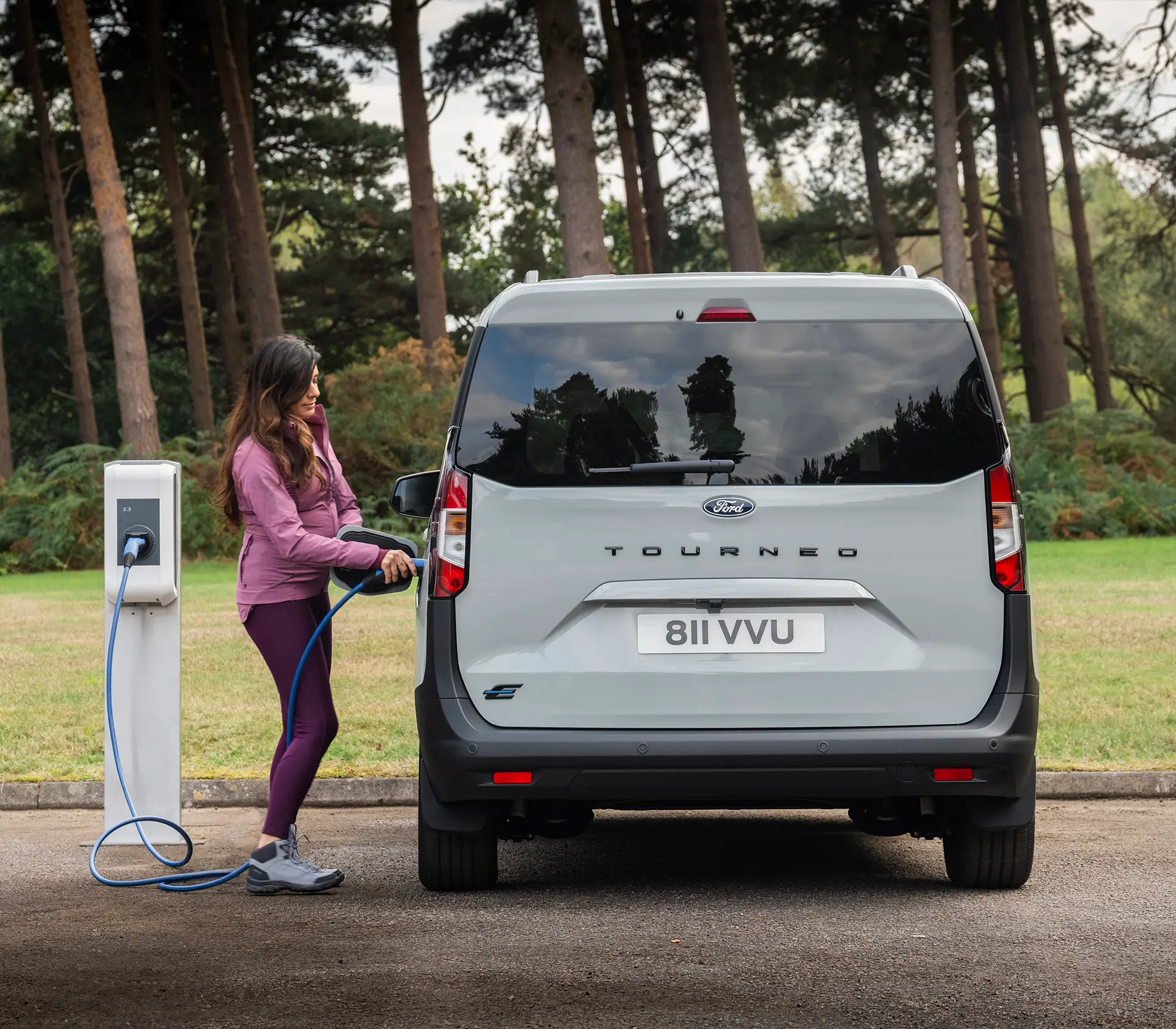 Frau läd grauen E-Tourneo Courier an der Ladesäule