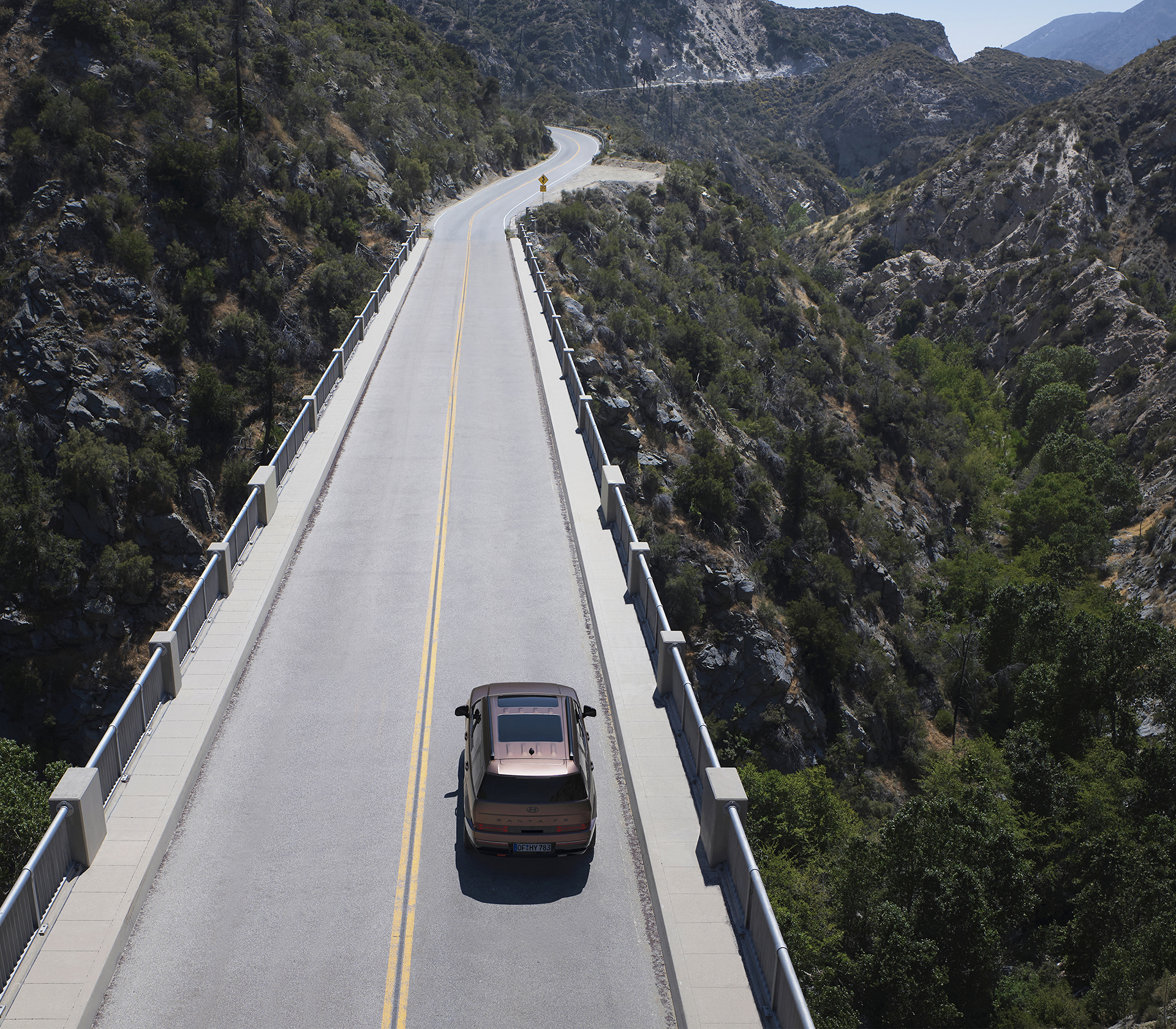 Hyundai SANTA FE  Anschicht von hinten und obenfährt auf einer Straße mit den Bergen und blauem Himmel im Hintergrund