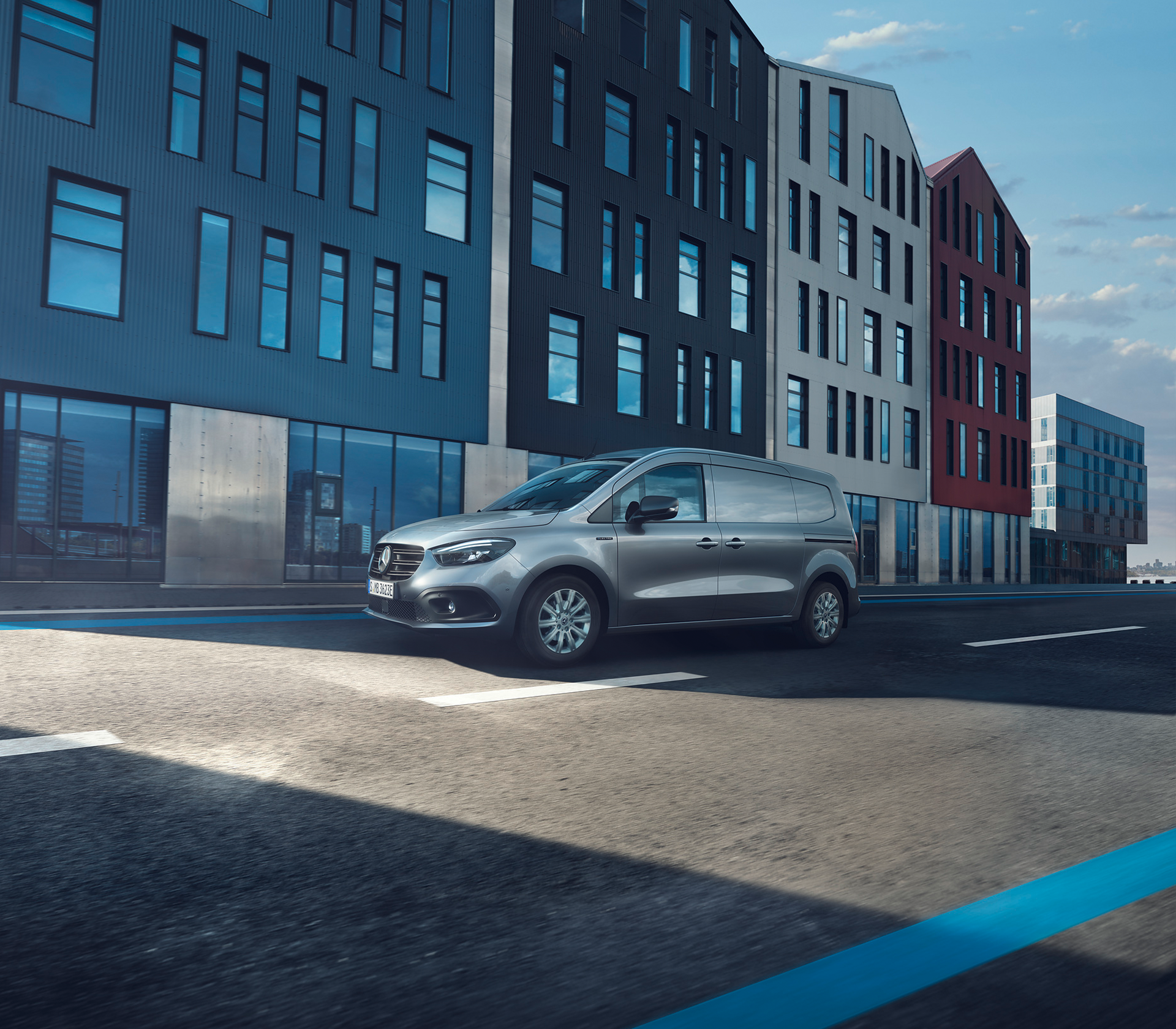 Moderner Mercedes-Benz Citan Kastenwagen in Silber fährt vor einer urbanen Architekturkulisse bei Tageslicht.
