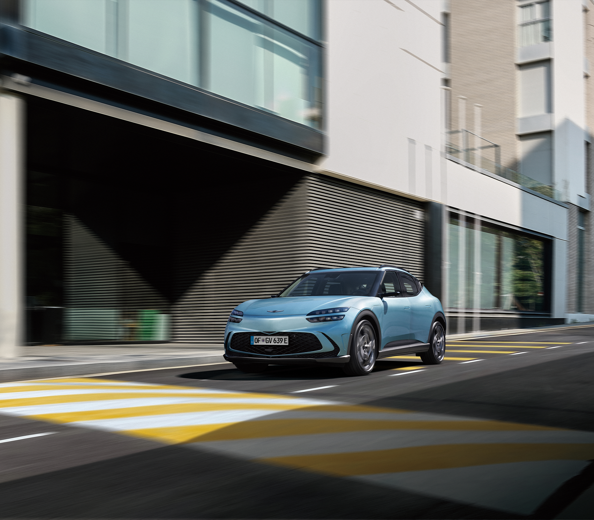 Genesis GV 60 fährt auf der Straüe und im Hintergrund sind moderne Gebäude