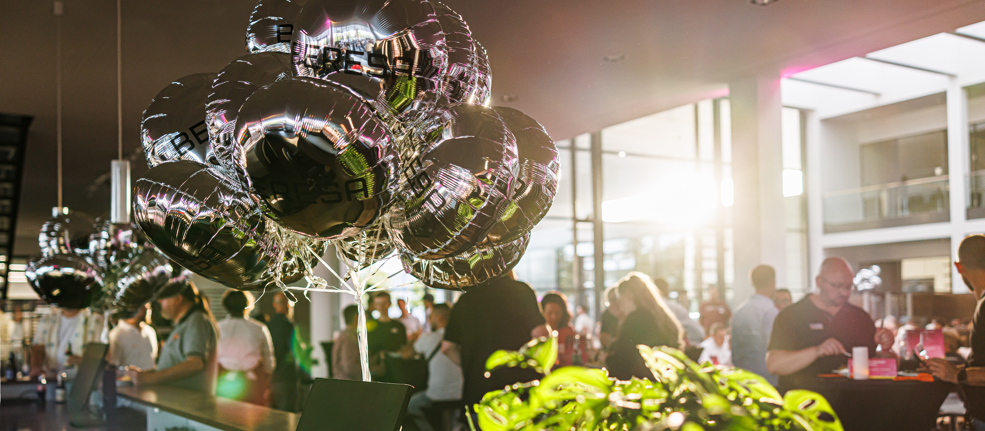 Runde BERESA Folienballons im Vordergrund und im Hintergrund sind Menschen zu sehen und der Sonnenuntergang, der durch die Fenster des Gebäudes scheint.